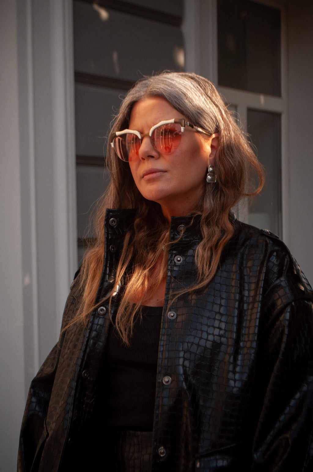 Жінка у чорному бомбері з глянцевої еко-шкіри з тисненням під крокодила; стильний чорний total look з міді-спідницею