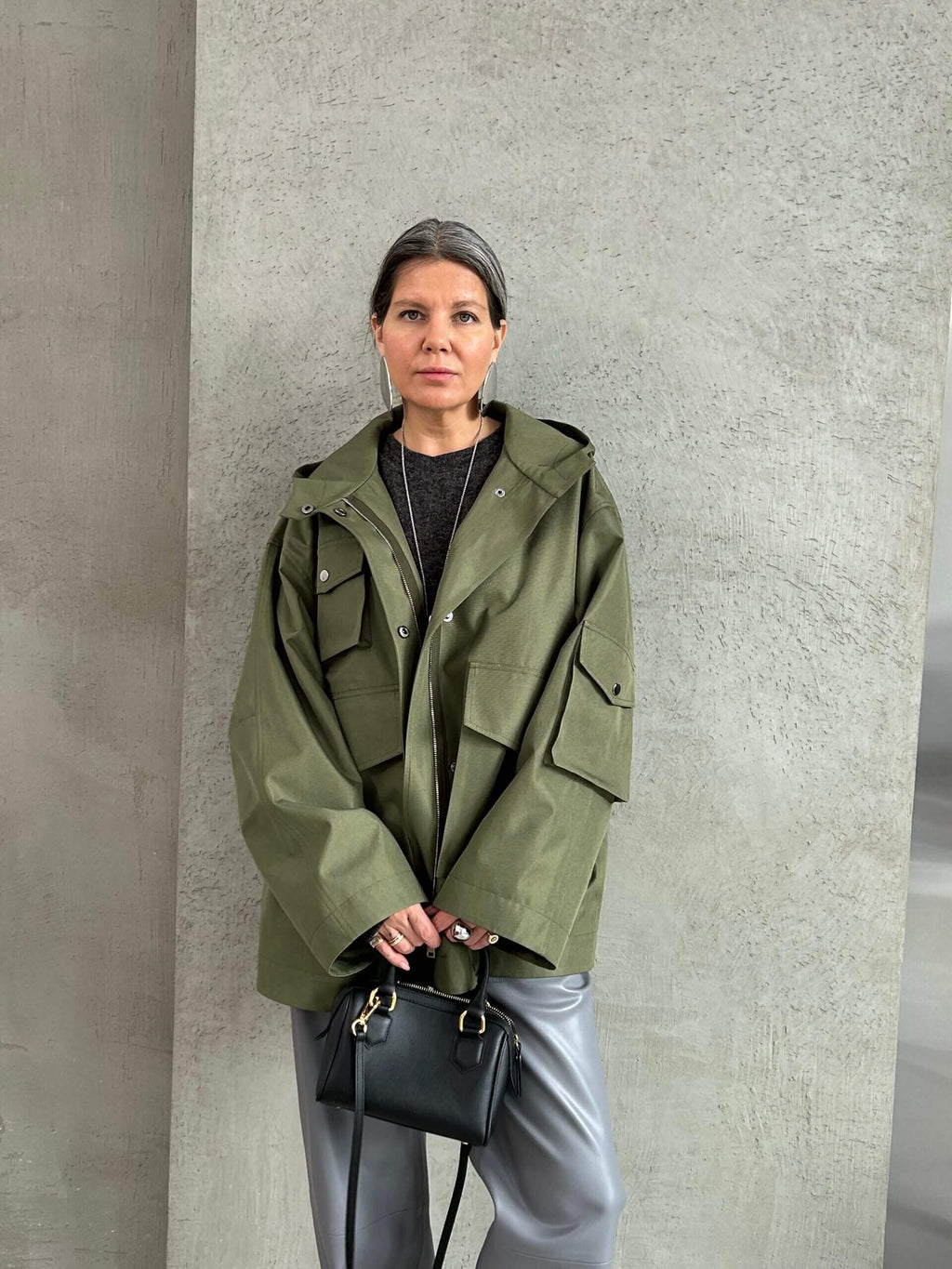 Жінка в оливковій oversize-парці з капюшоном, стильний міський легкий верхній одяг;